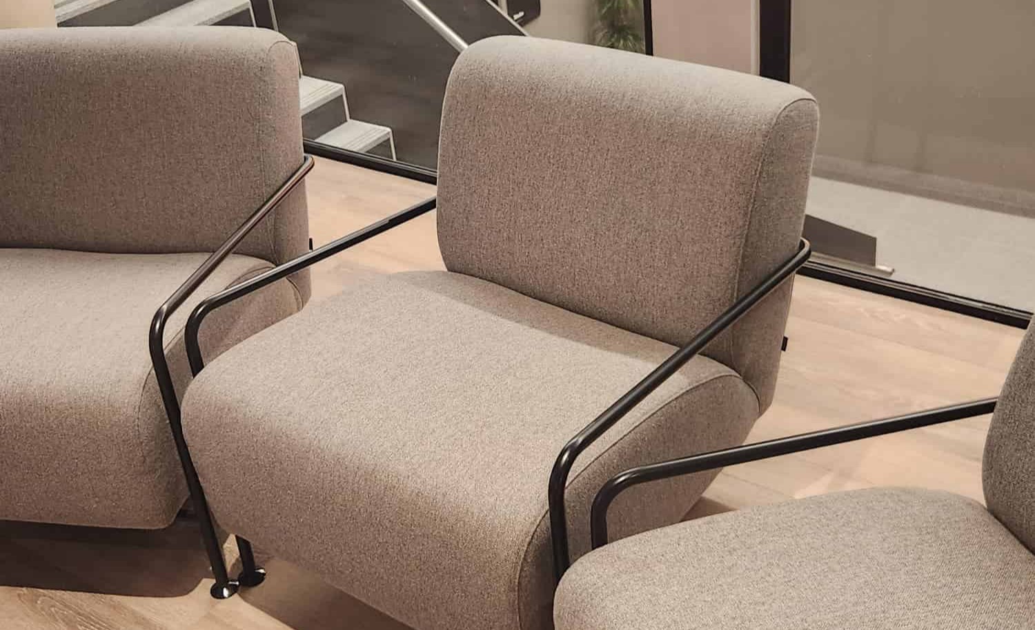 A row of modern lounge chairs with heather-gray upholstery and sleek, matte black metal frames on a light wood floor in a contemporary office setting.